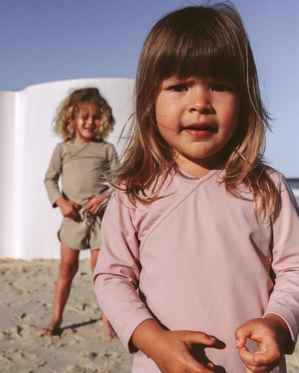 A little girl named Ada is standing on the beach wearing a Ada Rash Shirt.