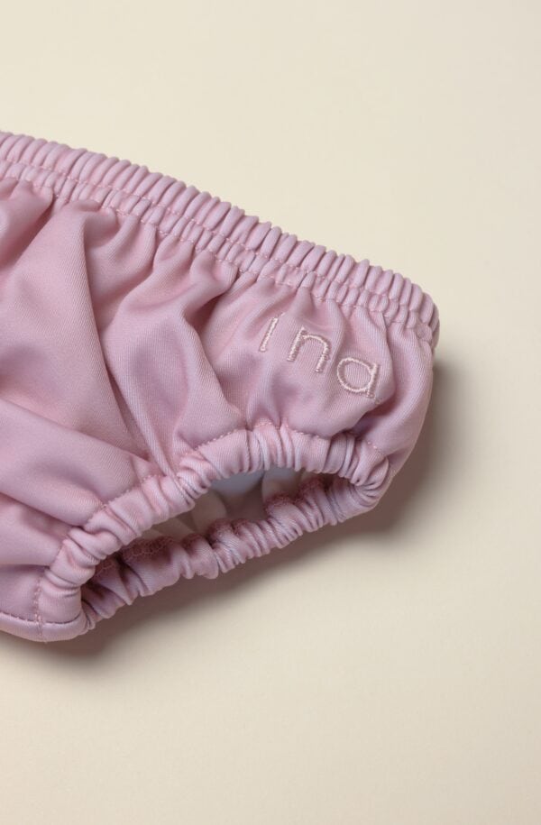 A close up of a pink Lumi Brief Swim Nappy on a white surface.