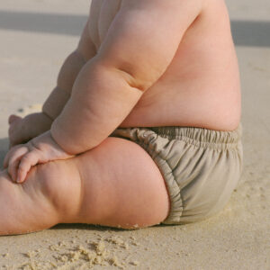 A baby wearing the Lumi Brief Swim Nappy sitting on the sand.