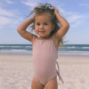 Mara, a little girl wearing a pink Mara One-Piece swimsuit, enjoys a day at the beach.