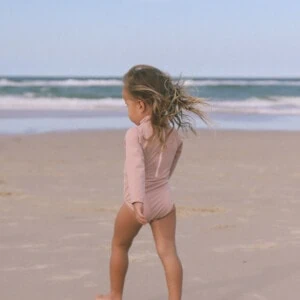 A little girl walking on the beach with her June Long Sleeve One-Piece blowing in the wind.