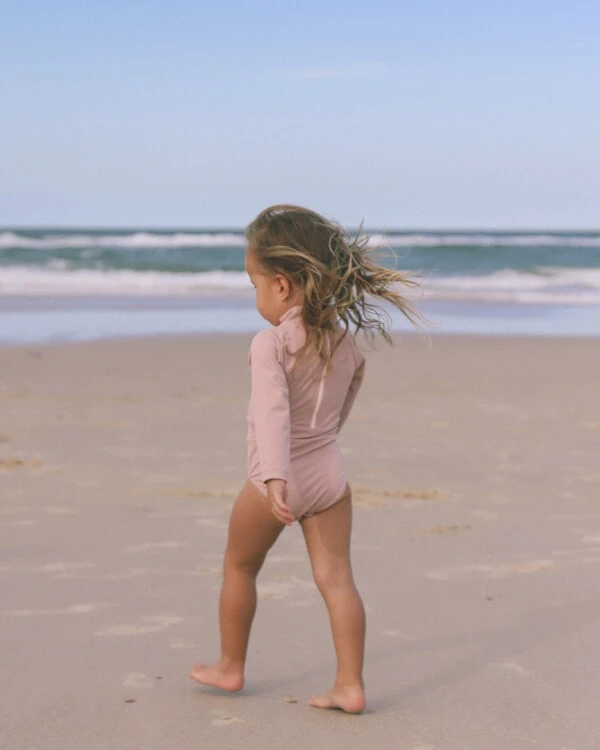 A little girl walking on the beach with her June Long Sleeve One-Piece blowing in the wind.