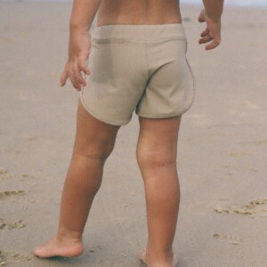 A child standing on the beach in Mesa Trunks.