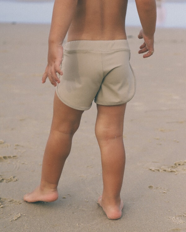A child standing on the beach in Mesa Trunks.