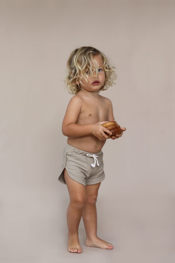 A young boy wearing Mesa Trunks shorts holding a doughnut.