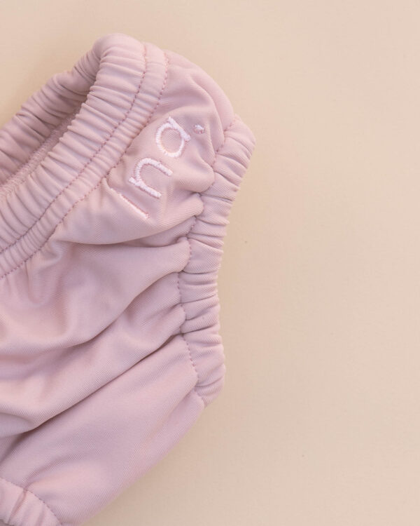A close up of a pink Lumi Brief Swim Nappy on a beige surface.