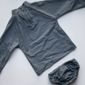 A grey long sleeved Lumi Brief Swim Nappy and pants on a white surface.