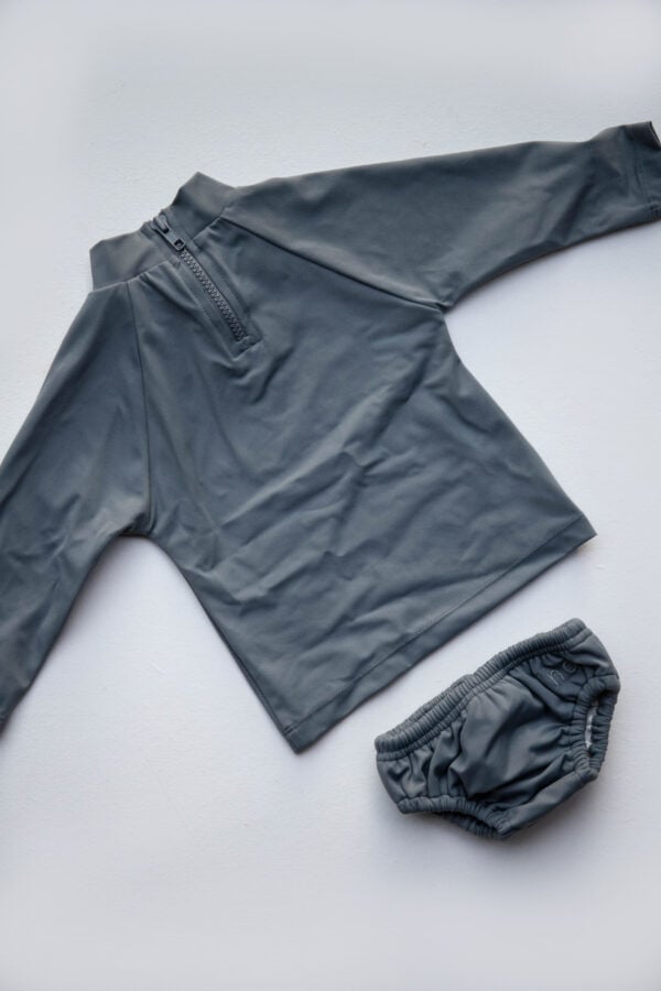 A grey long sleeved Lumi Brief Swim Nappy and pants on a white surface.