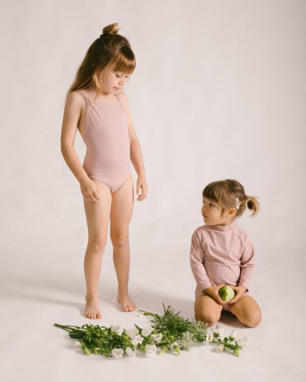 Two little girls standing next to each other in a pink Mara One-Piece.