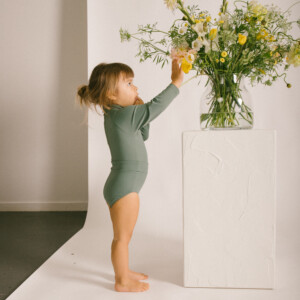 A little girl is standing in front of the Essentials Range - June One-Piece - Moss Colour.