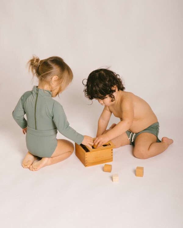 Two children playing with the Essentials Range - June One-Piece - Moss Colour on a white background.