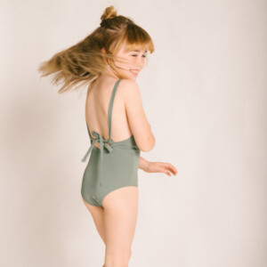 Mara, a little girl, wearing a green swimsuit, specifically the Mara One-Piece design.