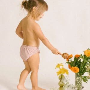 A little girl in a Lumi Brief Swim Nappy playing with flowers.