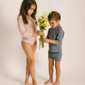 Two children standing next to each other holding the June Long Sleeve One-Piece.
