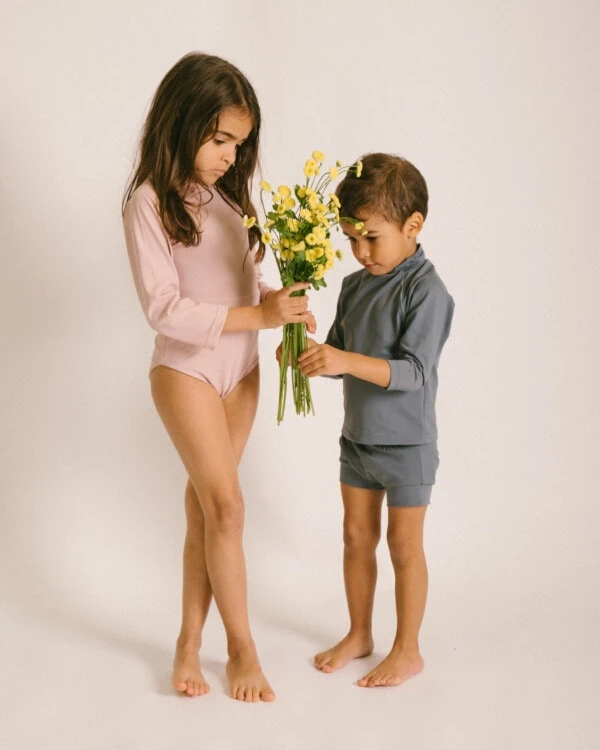 Two children standing next to each other holding the June Long Sleeve One-Piece.