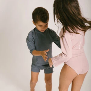 A boy and a girl in the June Long Sleeve One-Piece bathing suit.