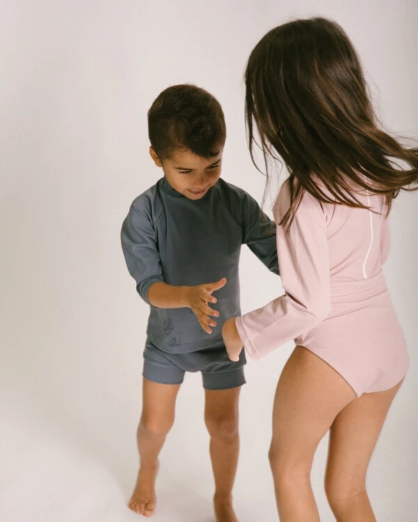 A boy and a girl in the June Long Sleeve One-Piece bathing suit.