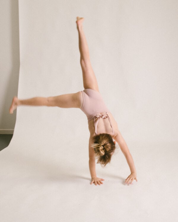 A young girl wearing the Lela One-Piece swimsuit confidently performs a handstand in a well-lit studio.