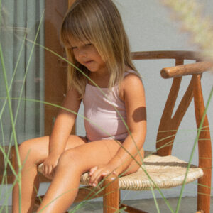 A little girl wearing a Mara One-Piece sitting on a wooden chair.