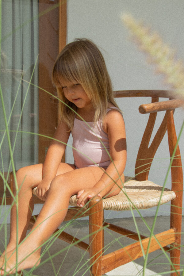 A little girl wearing a Mara One-Piece sitting on a wooden chair.