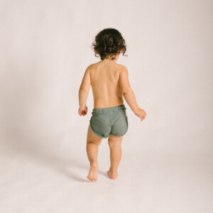 A baby is walking in a studio wearing Mesa Trunks.