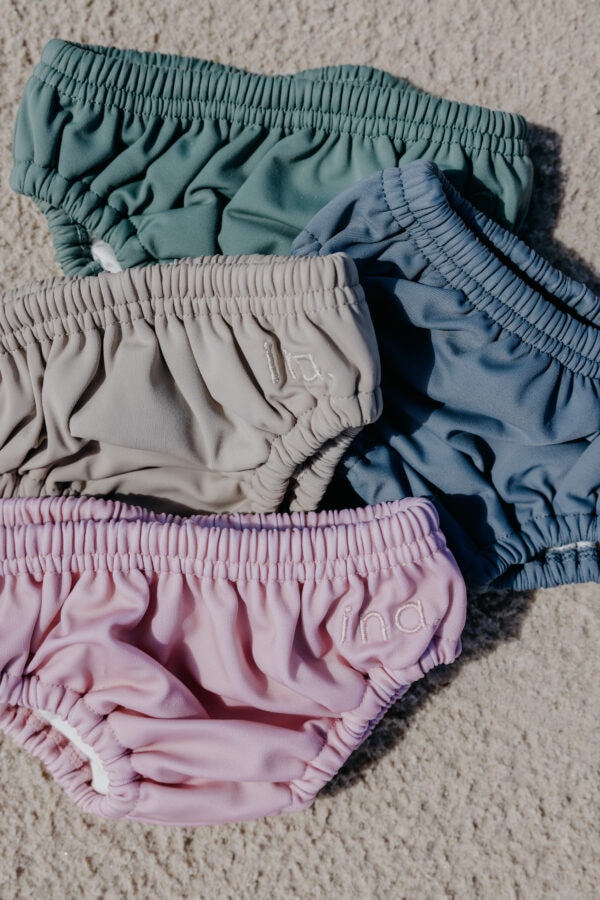 Four different colors of Lumi Brief Swim Nappies laying on top of a carpet.