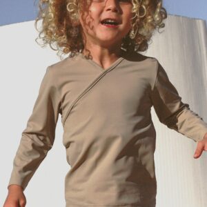 A young girl wearing the Essentials Range - Ada Rash Shirt in Sand Colour and shorts.