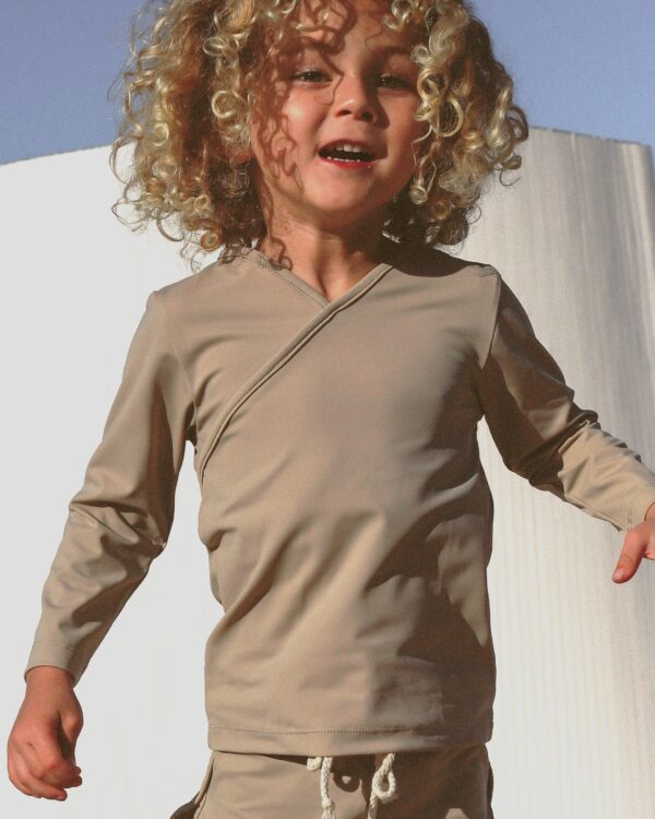 A young girl wearing the Essentials Range - Ada Rash Shirt in Sand Colour and shorts.