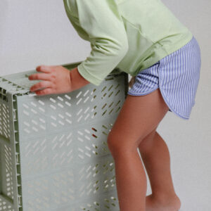 A little girl reaching into a Playtime Collection - Mesa Trunks - Berry Stripe.