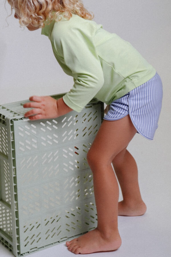 A little girl reaching into a Playtime Collection - Mesa Trunks - Berry Stripe.