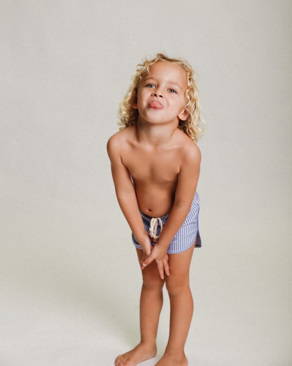 A young boy in Playtime Collection - Mesa Trunks - Berry Stripe posing for a photo.