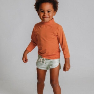 A young boy wearing the Playtime Collection - Nella Rash Shirt - Mandarin and shorts.