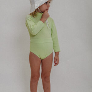 A little girl wearing a Playtime Collection - June Long Sleeve One-Piece - Melon swimsuit and white hat.