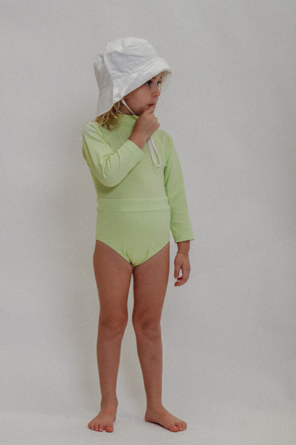 A little girl wearing a Playtime Collection - June Long Sleeve One-Piece - Melon swimsuit and white hat.