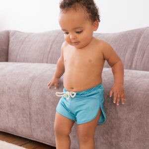 A baby in Sorbet Summer - Nella Rash Shirt shorts standing on a couch.