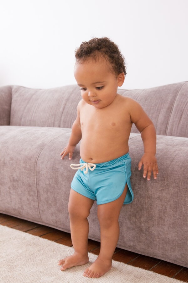 A baby in Sorbet Summer - Nella Rash Shirt shorts standing on a couch.