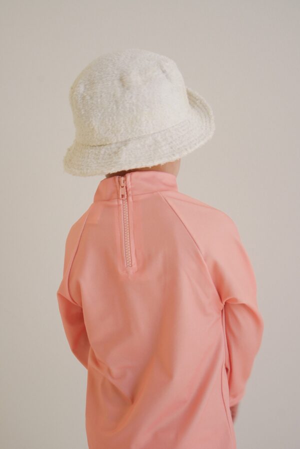 A child wearing a white hat and a pink Sorbet Summer - Nella Rash Shirt jacket.
