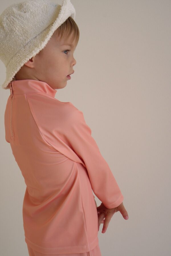 A young boy wearing a hat and the Sorbet Summer - Nella Rash Shirt.