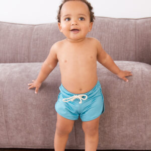 A baby in Sorbet Summer - Mesa Trunks standing on a couch.
