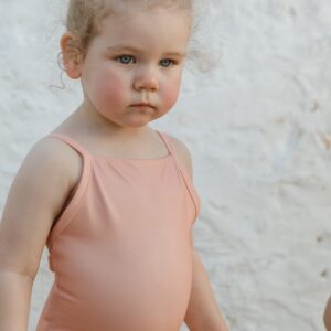 A little girl in a Sorbet Summer - Mara One-Piece swimsuit standing next to a white wall.