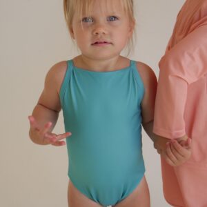 A little girl in a Sorbet Summer - Mara One-Piece swimsuit and pink hat.