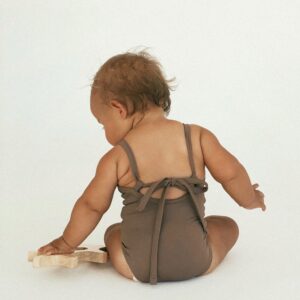 A baby in a Mara One-Piece swimsuit sitting on a wooden board.