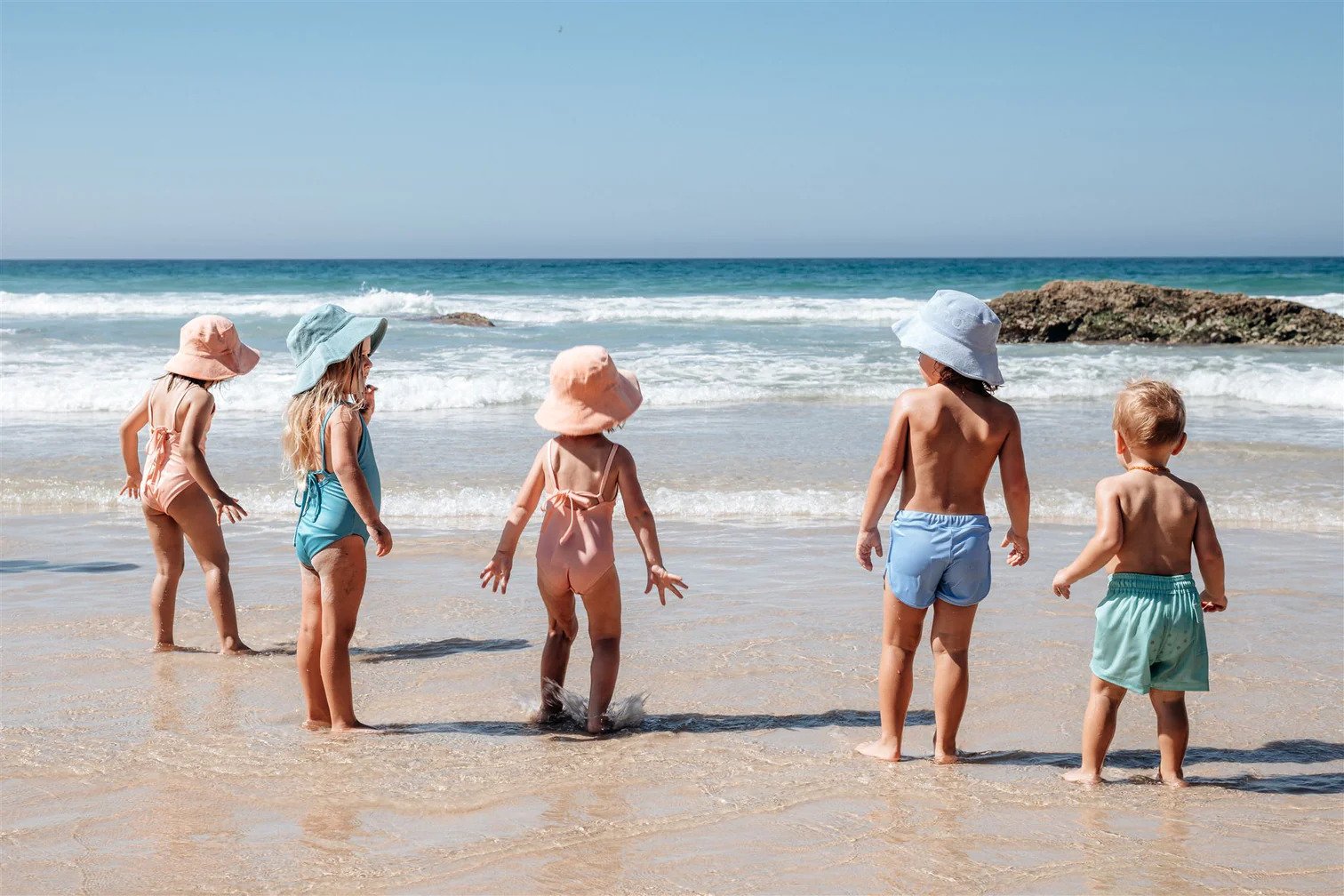 A group of children standing on the beach in eco-friendly swimwear.