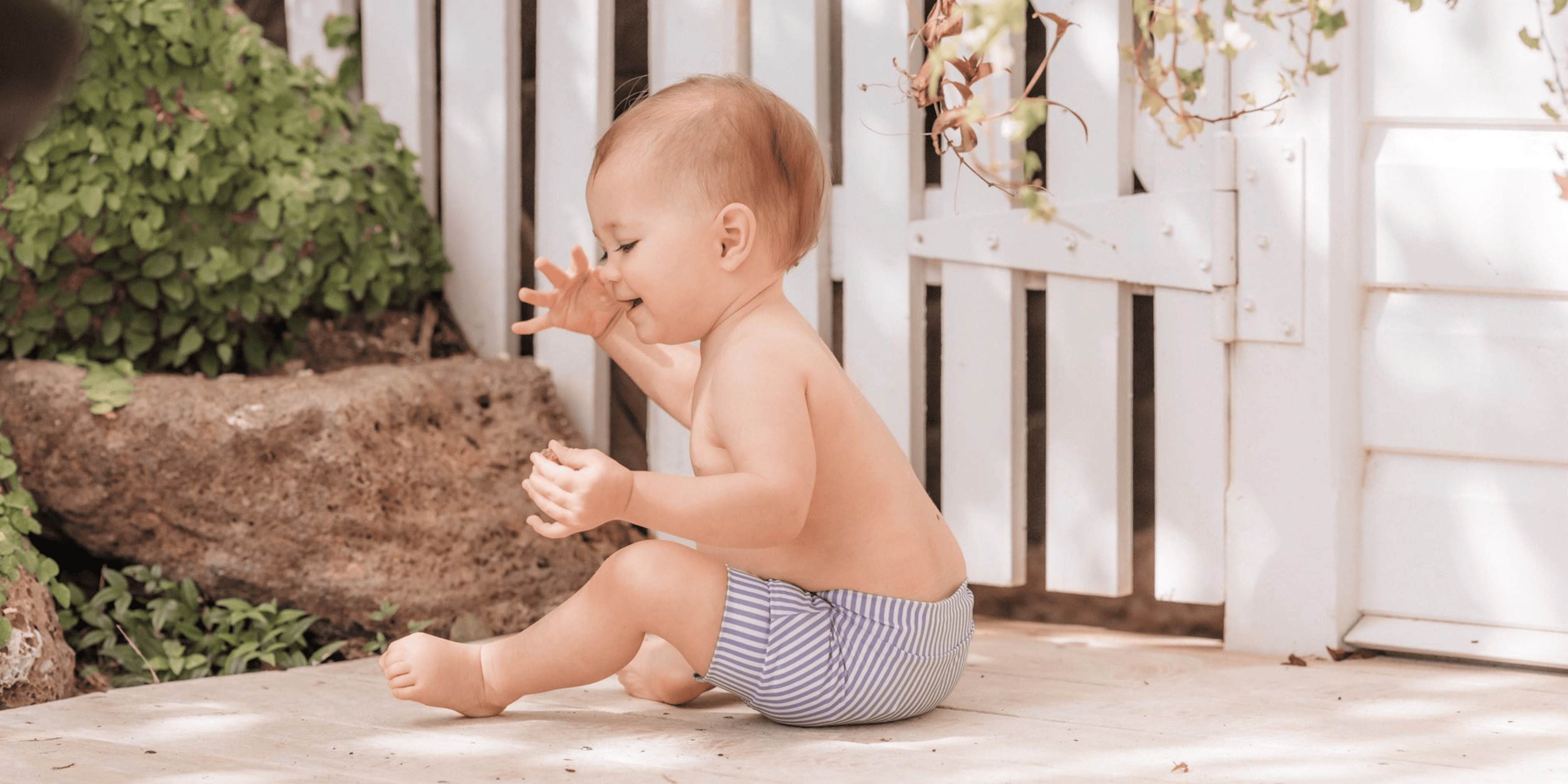 A baby is sitting on the ground in front of a sustainable, eco-friendly fence.