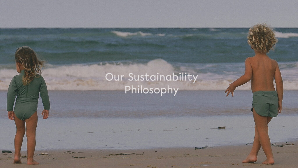 Two children standing on the beach wearing sustainable swimwear.