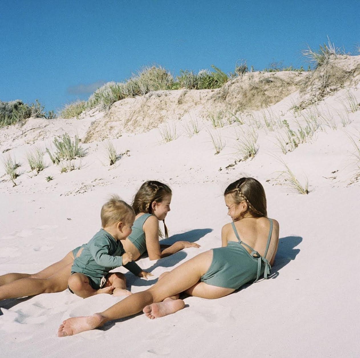 Three children wearing eco-friendly swimwear laying on the sand.