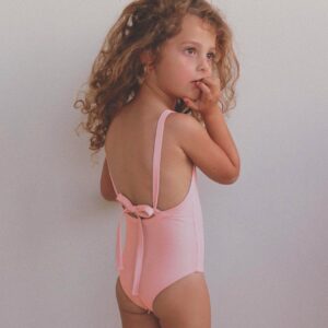 A little girl wearing a pink one piece swimsuit.