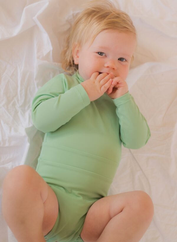 A baby in a Retro Wave By Ina - June One-Piece bodysuit laying on a bed.
