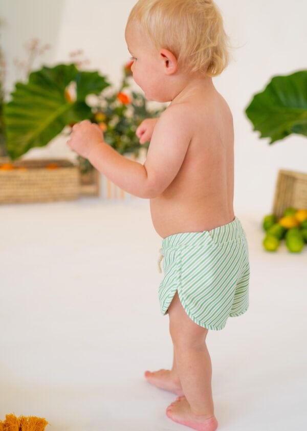 A baby is standing in a Retro Wave By Ina - Mesa Trunks swim short.