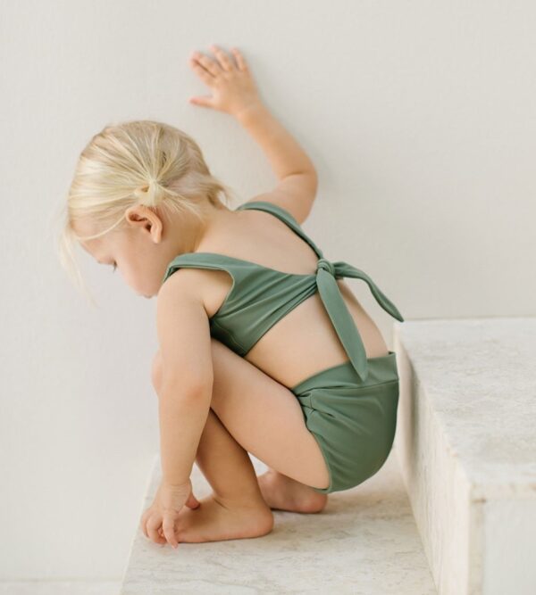 A little girl in a green bikini sitting on a step.